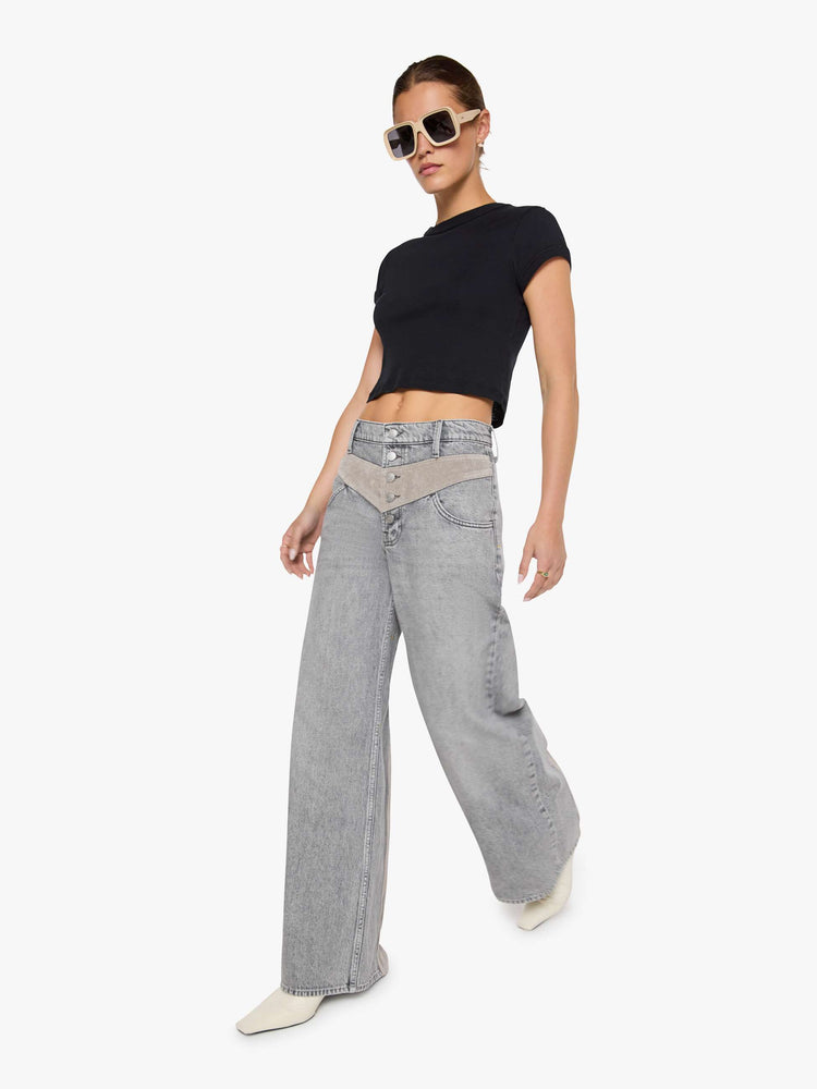 Walking view view of a woman in a washed grey high-rise pants are designed with an inset corduroy panel at the waist and down the back legs, an exposed button fly, low-slung fit and a 30-inch inseam with a clean hem.