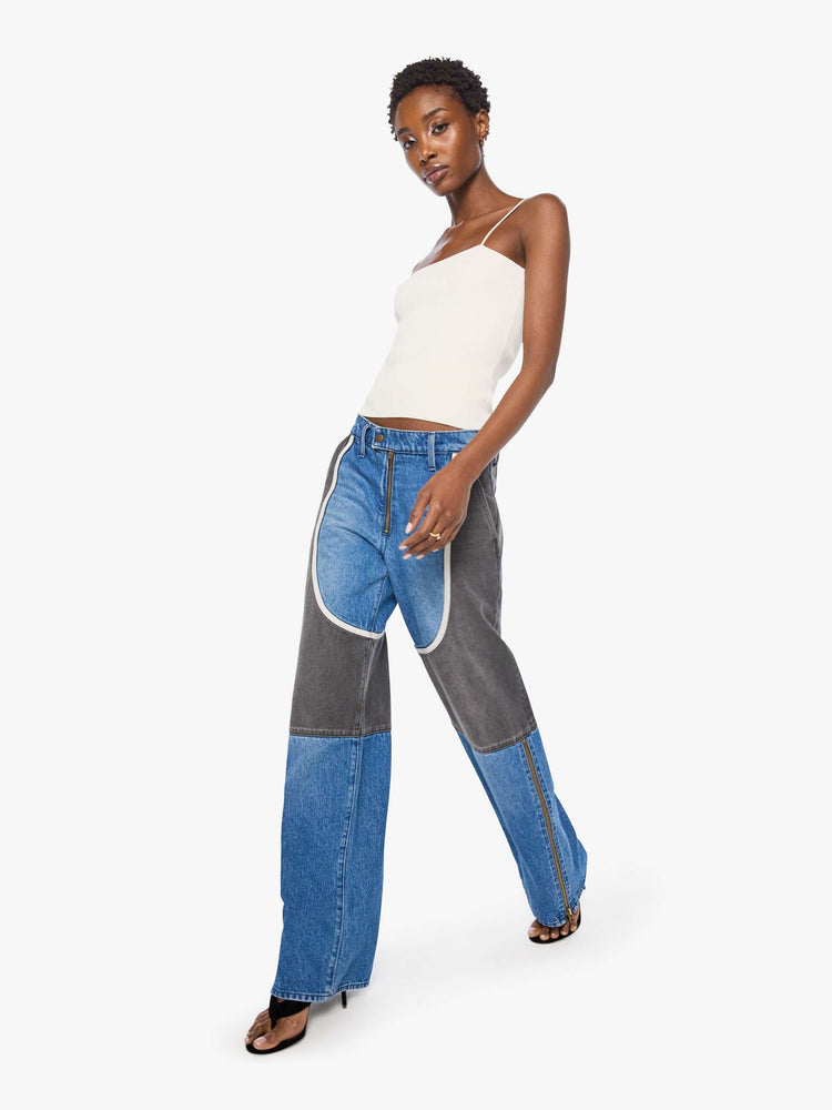 Walking view of a woman in mid blue with moto-inspired panels in faded black with white trim at the hips wide-leg jeans are designed with an exposed zip fly, button-tab waistband, side slit pockets, a zipper down the outer calf seam and a long 32-inch inseam with a clean hem.