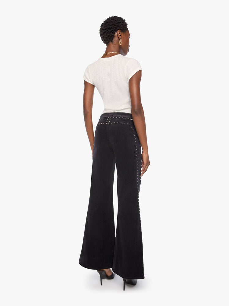 Back view of a woman in a black corduroy high-waisted wide-leg pants with a button fly, adjustable details at the waistband, a 31-inch inseam and clean hem.