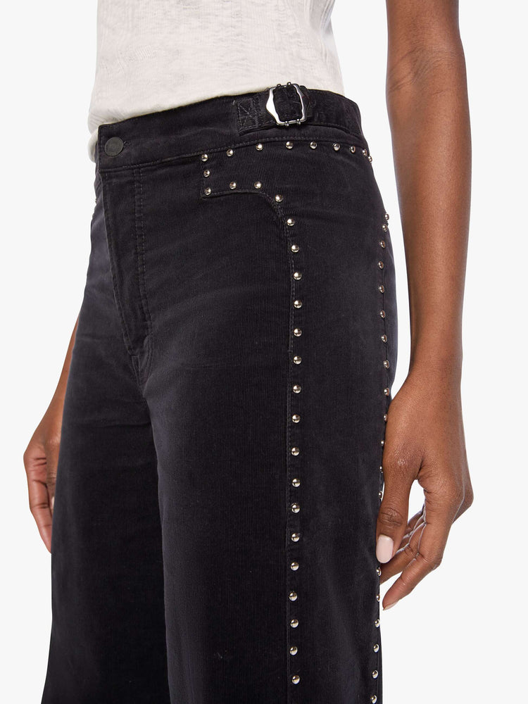 Close up view of a woman in a black corduroy high-waisted wide-leg pants with a button fly, adjustable details at the waistband, a 31-inch inseam and clean hem.