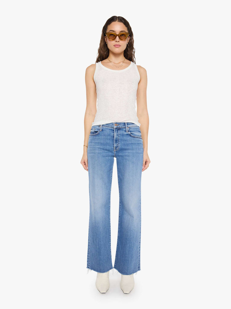Front view of a woman in a med blue mid-rise jeans with a loose fit, wide leg, zip fly and a 31-inch inseam with a frayed hem.