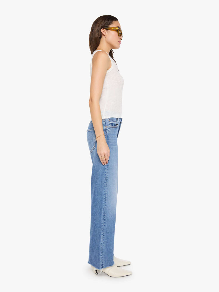 Side view of a woman in a med blue mid-rise jeans with a loose fit, wide leg, zip fly and a 31-inch inseam with a frayed hem.