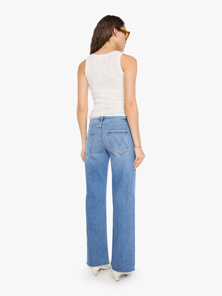 Back view of a woman in a med blue mid-rise jeans with a loose fit, wide leg, zip fly and a 31-inch inseam with a frayed hem.