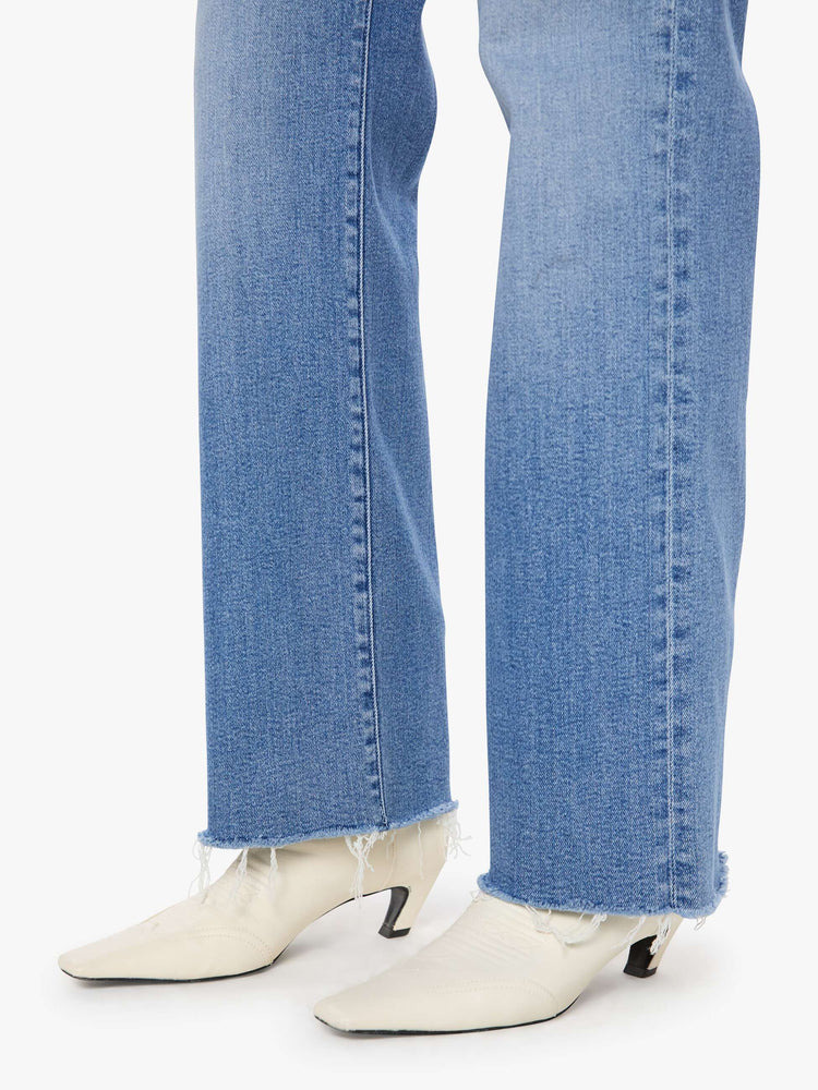 Close up hem view of a woman in a med blue mid-rise jeans with a loose fit, wide leg, zip fly and a 31-inch inseam with a frayed hem.