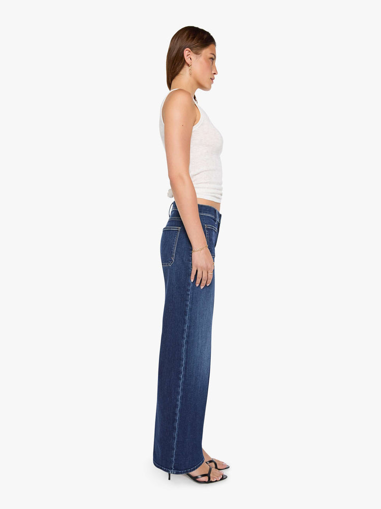Side view of a woman in a dark blue mid-rise jeans with a loose fit, wide leg, patch pockets, zip fly and 32-inch inseam with a clean hem.