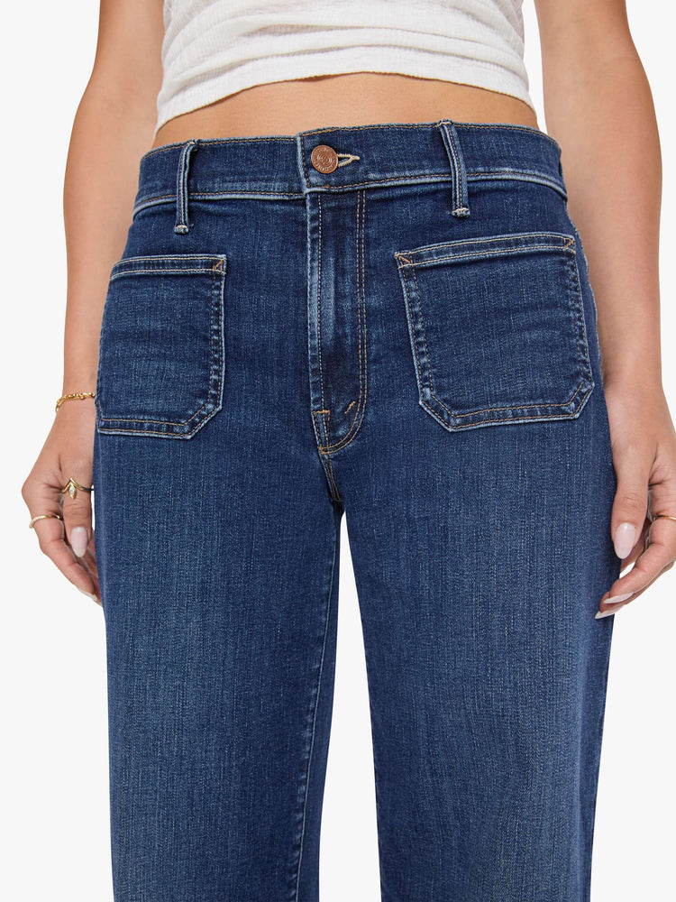Close up view of a woman in a dark blue mid-rise jeans with a loose fit, wide leg, patch pockets, zip fly and 32-inch inseam with a clean hem.