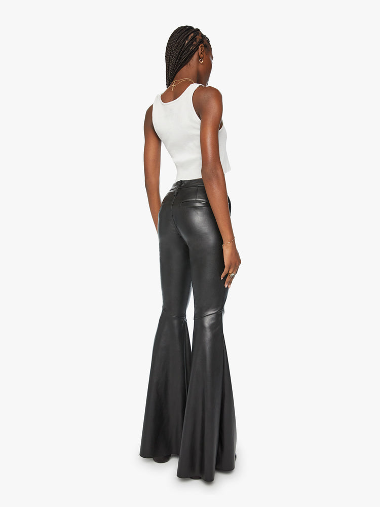 Back view of a woman mid rise pants with diagonal seams at the knees, a super-wide flare and an extra-long 35-inch inseam in a faux black leather.