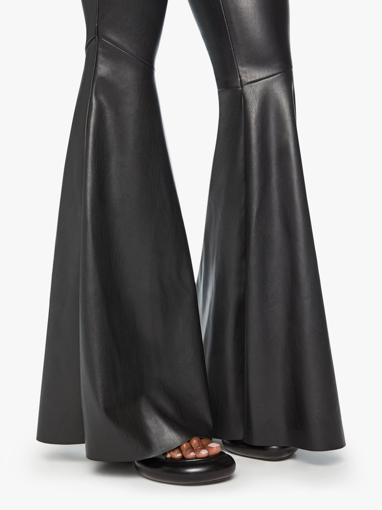 Hem view of a woman mid rise pants with diagonal seams at the knees, a super-wide flare and an extra-long 35-inch inseam in a faux black leather.