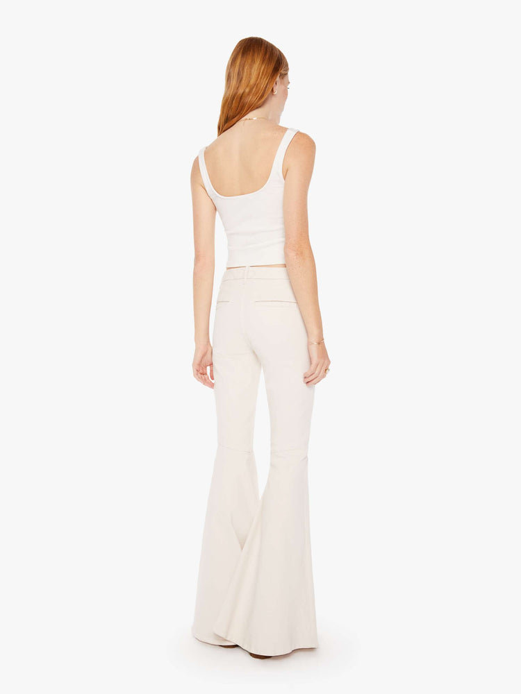 Back view of a woman high-rise pants with diagonal seams at the knees, a super-wide flare, slit pockets and an extra-long 35-inch inseam in a light khaki cream.