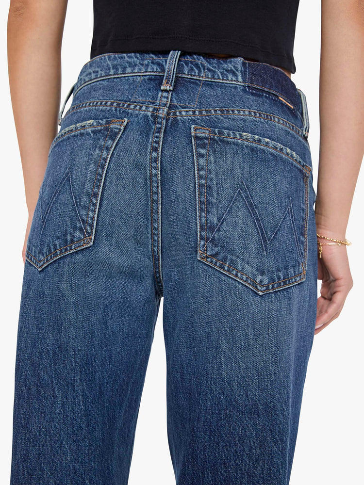 Close up view of a woman in a med blue jeans designed to sit on the hips with a slouchy fit, a loose straight leg, zip fly and a 34-inch inseam with a clean hem. 