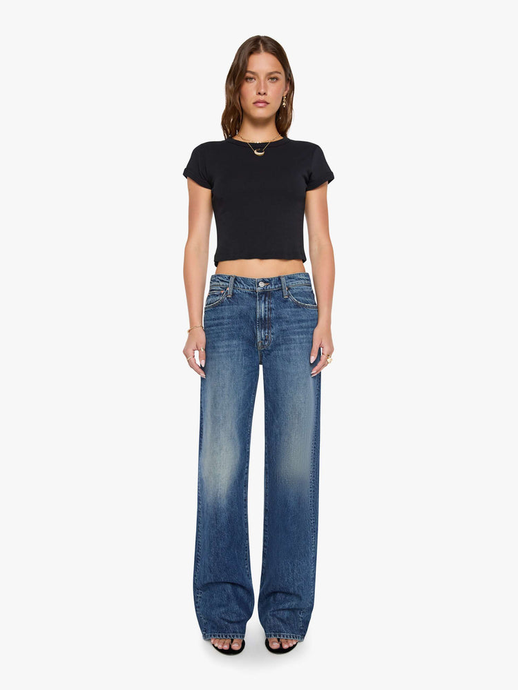 Front view of a woman in a med blue jeans designed to sit on the hips with a slouchy fit, a loose straight leg, zip fly and a 34-inch inseam with a clean hem. 