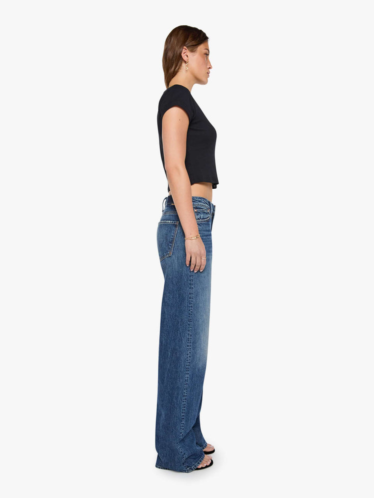 Side view of a woman in a med blue jeans designed to sit on the hips with a slouchy fit, a loose straight leg, zip fly and a 34-inch inseam with a clean hem. 