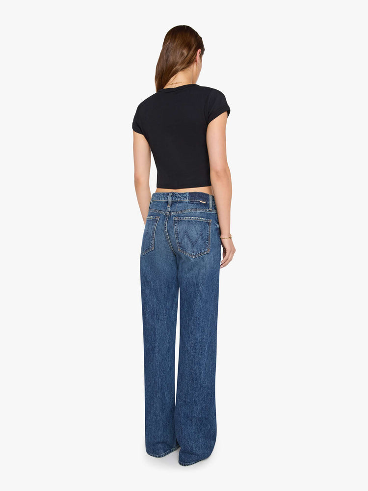 Back view of a woman in a med blue jeans designed to sit on the hips with a slouchy fit, a loose straight leg, zip fly and a 34-inch inseam with a clean hem. 