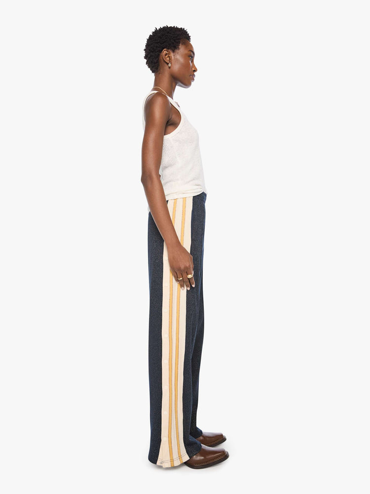 Side  view of a woman in a metallic navy with cream and golden yellow stripes down the legs wide-leg track pants with an elastic waistband, loose leg and a contrast side stripe with buttons down the outer seams. 