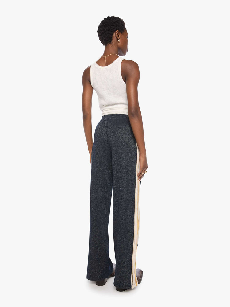 Back  view of a woman in a metallic navy with cream and golden yellow stripes down the legs wide-leg track pants with an elastic waistband, loose leg and a contrast side stripe with buttons down the outer seams. 
