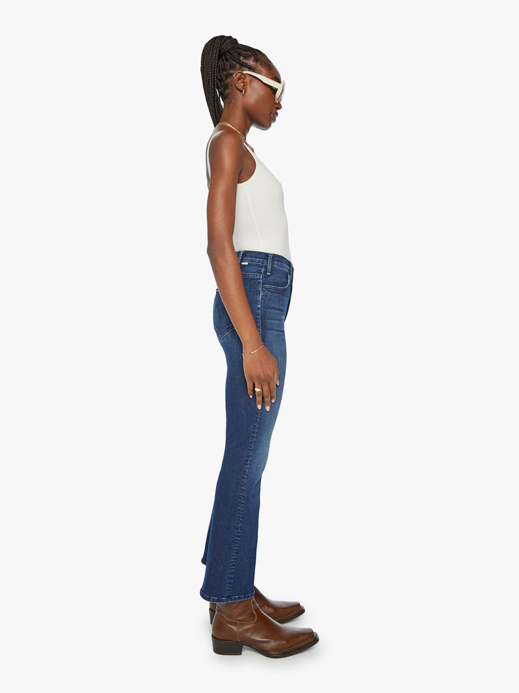 Side view of a woman in high-rise flare has an ankle-length inseam and a clean hem in a dark blue wash.