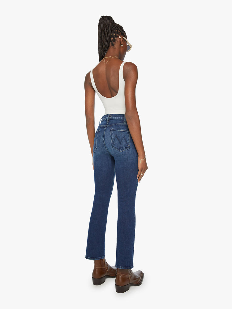 Back view of a woman in high-rise flare has an ankle-length inseam and a clean hem in a dark blue wash.