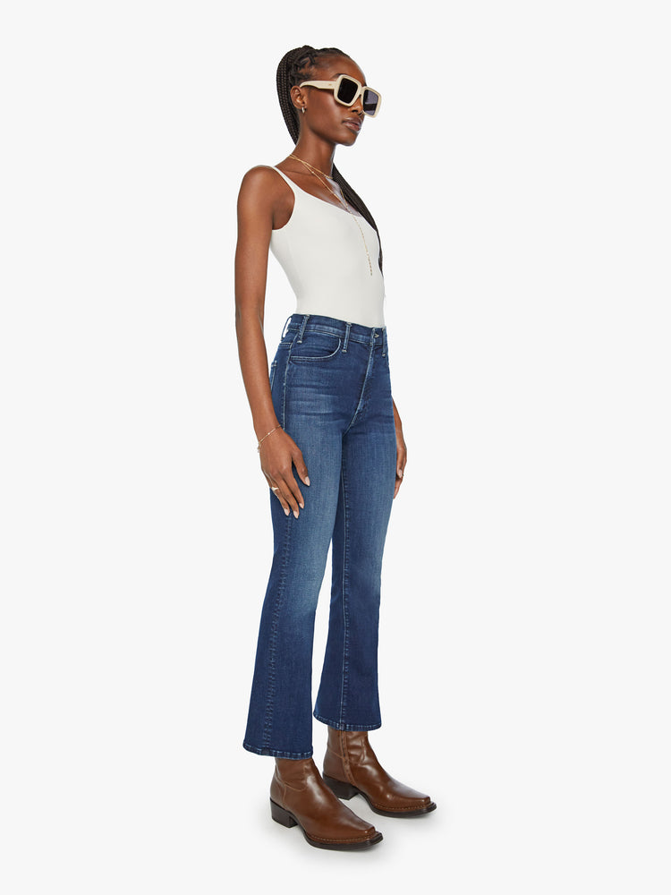 Side angle view of a woman in high-rise flare has an ankle-length inseam and a clean hem in a dark blue wash.