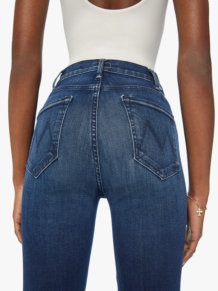 Back close up view of a woman in high-rise flare has an ankle-length inseam and a clean hem in a dark blue wash.