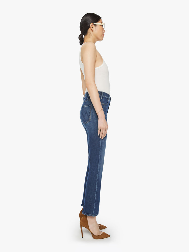 Side view of a woman high-rise flare has an ankle-length inseam and a clean hem in a dark blue wash.