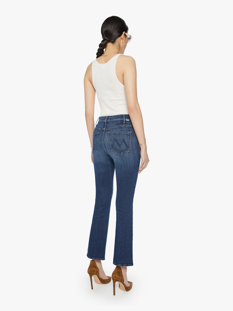 BacK view of a woman high-rise flare has an ankle-length inseam and a clean hem in a dark blue wash.