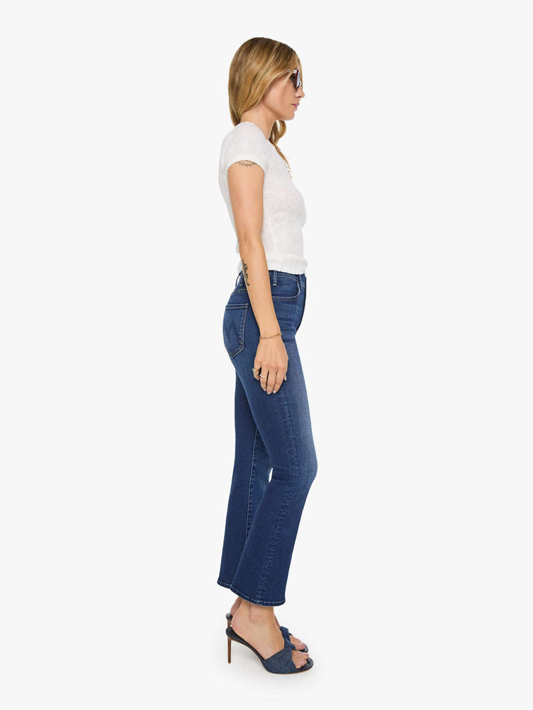 Side view of a woman in a dark blue high-rise flare jean with an ankle-length inseam and a clean hem.