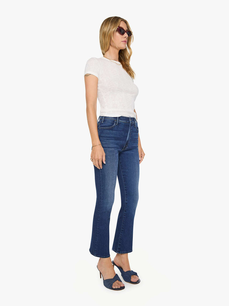 Side angle view of a woman in a dark blue high-rise flare jean with an ankle-length inseam and a clean hem.
