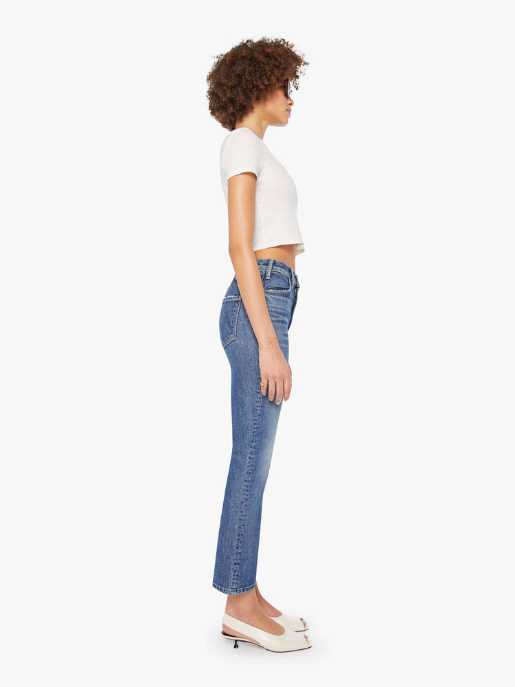 Side view of a woman in a mid-blue high-rise flare has a zip fly, ankle-length inseam and a clean hem.