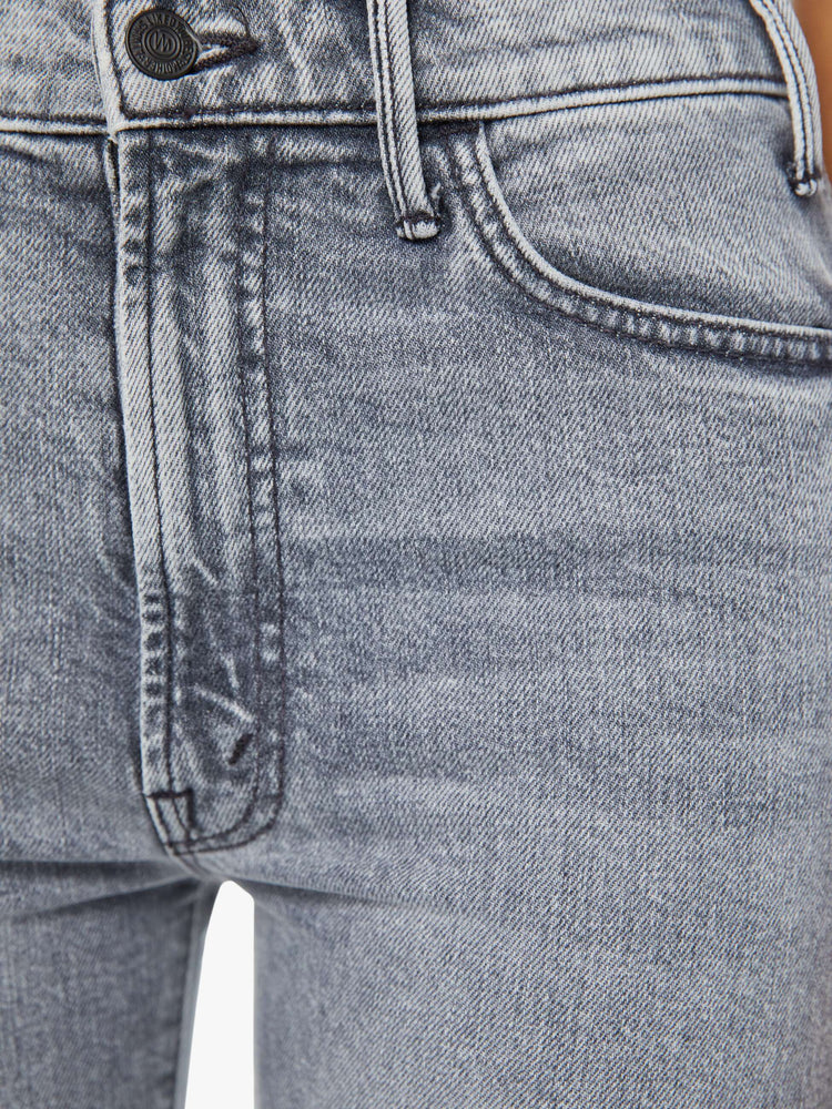 Detailed view of a woman in light-grey high-rise flare that has an ankle-length inseam and a clean hem with whiskering and fading plus a matte black button.