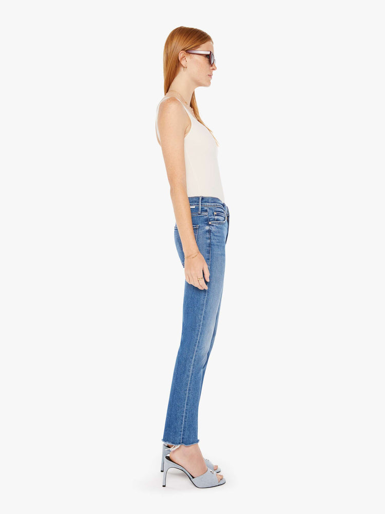 Side view of a womens medium blue wash jean featuring a mid rise, straight leg, and a ankle length frayed hem.