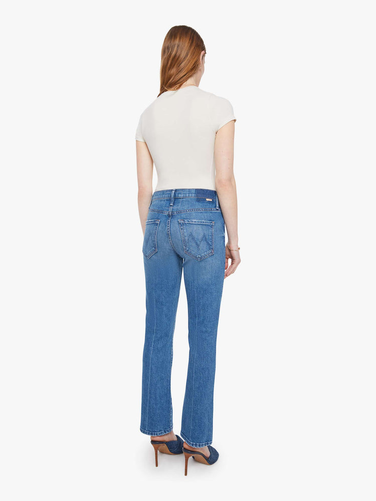 Back view of a woman in a mid blue high-rise bootcut has an ankle-length inseam, zip fly and a clean hem.