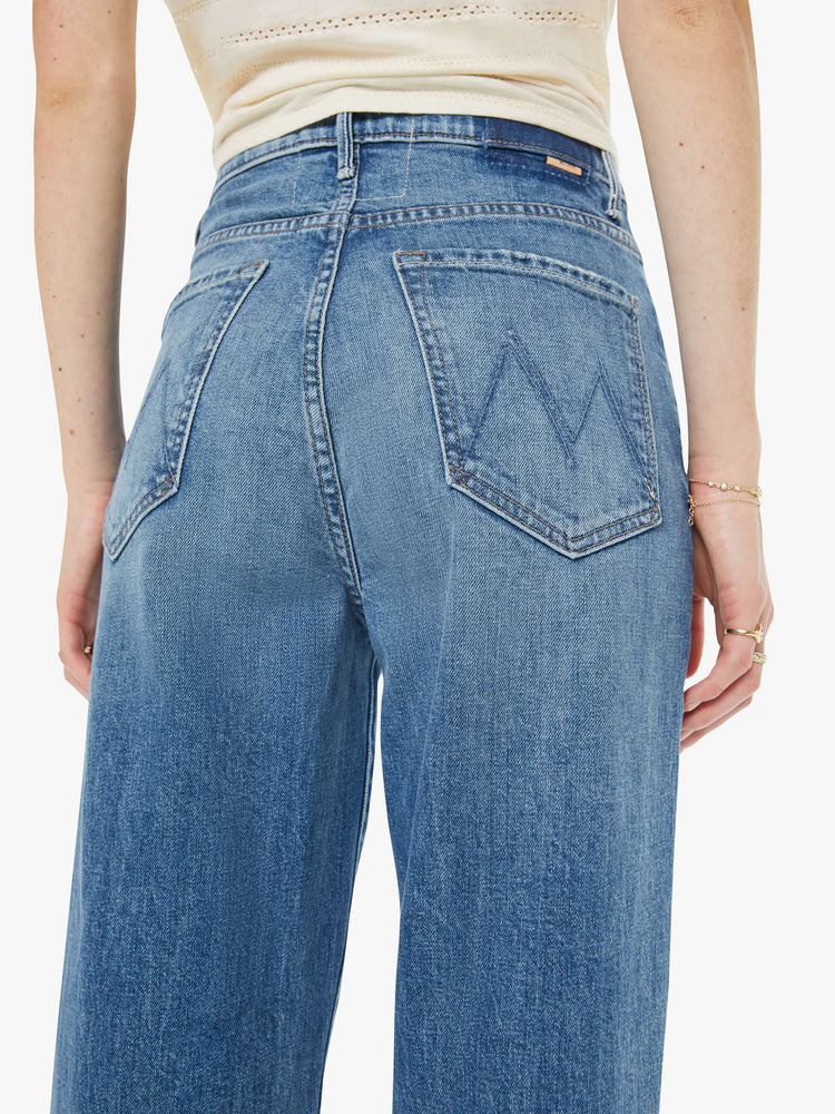 Close up view of a woman in a med blue super high-waisted wide-leg jeans with a zip fly, long 32-inch inseam and a clean hem.