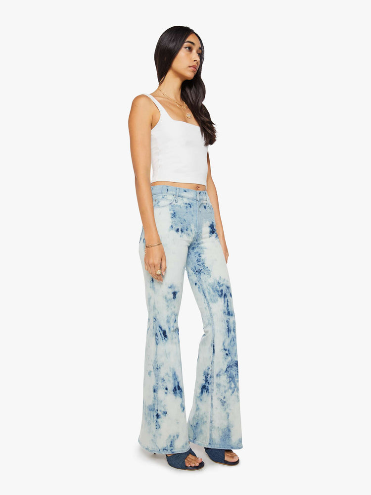 Side angle view of a woman in a bleach-dyed light blue with darker and lighter spots throughout high-rise flare jean with a zip fly, long 34-inch inseam and a clean hem. 