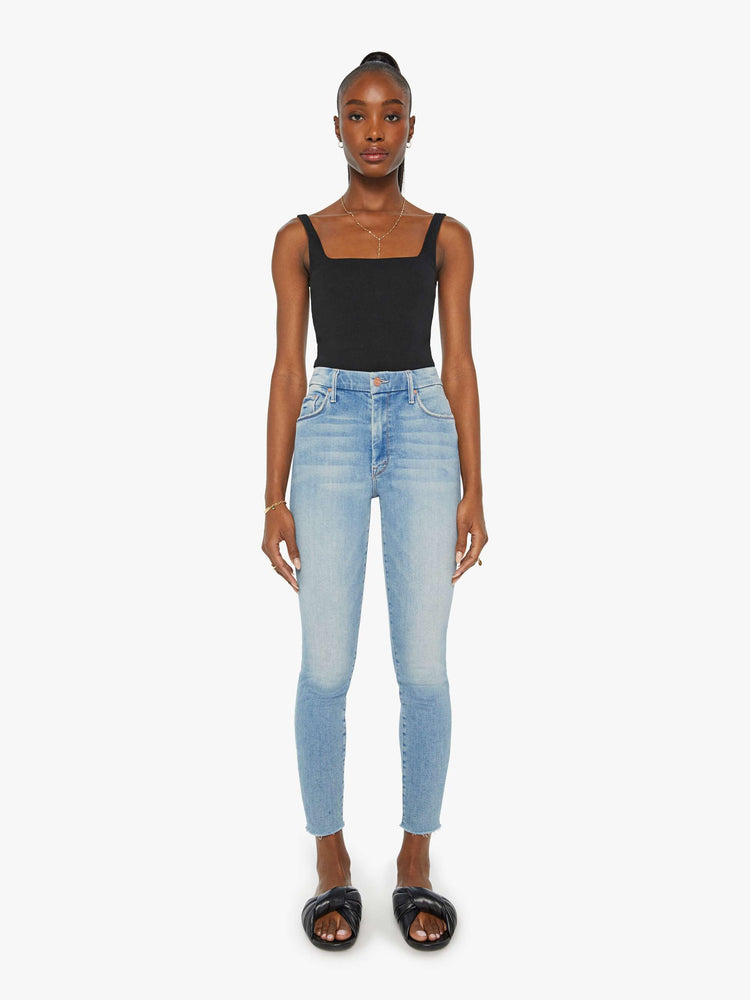 Front view of a womens light blue jean featuring a high rise a skinny fit, and a raw ankle fray.