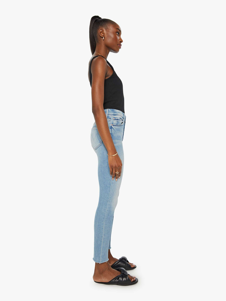 Side view of a womens light blue jean featuring a high rise a skinny fit, and a raw ankle fray.