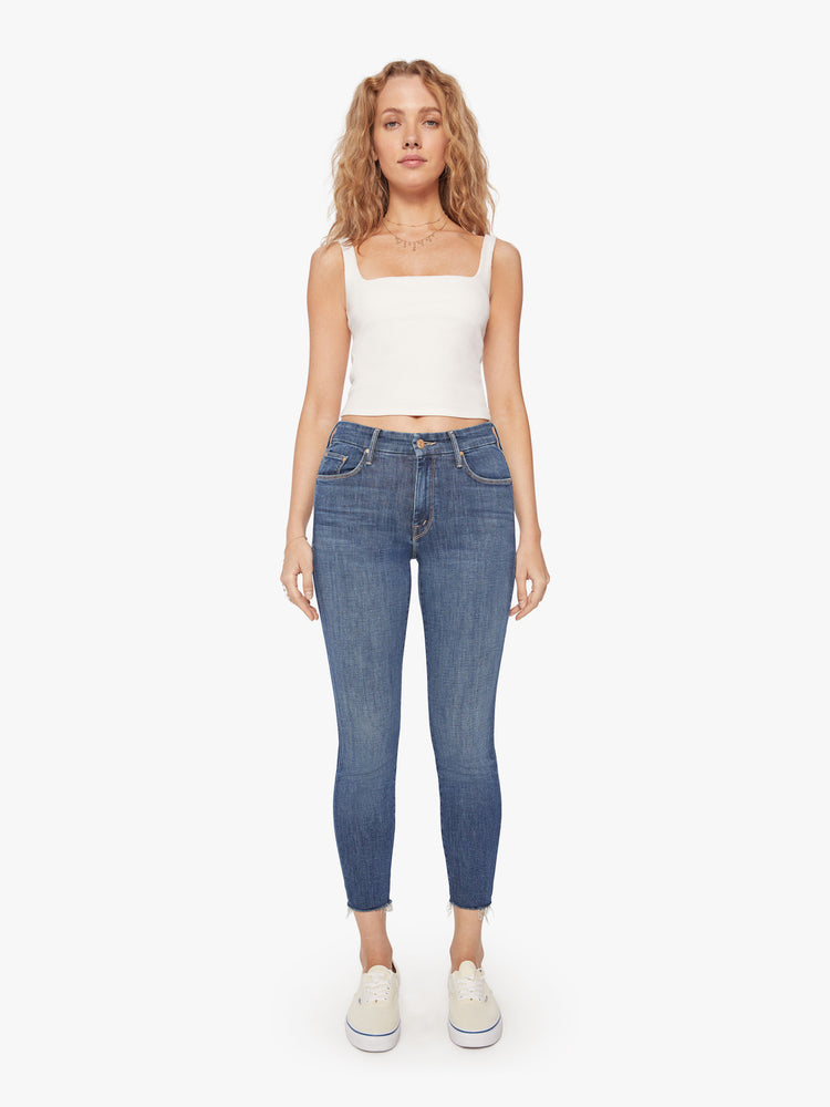 Front view of a womens mid rise jean in a medium blue wash, featuring a skinny, raw cut ankle hem.