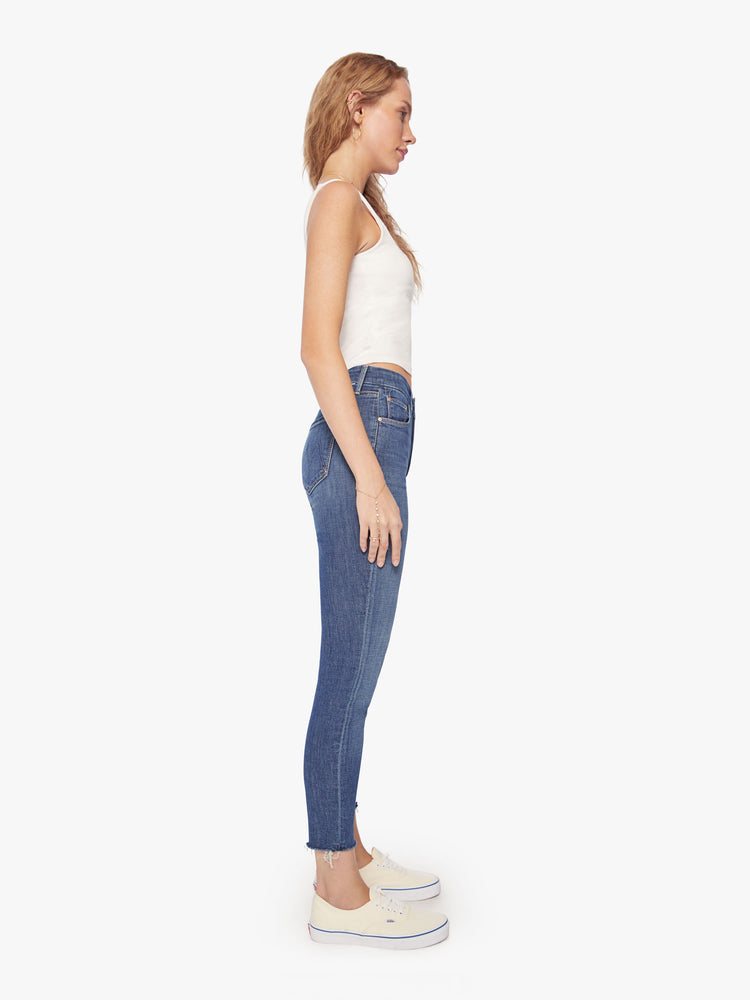 Side view of a womens mid rise jean in a medium blue wash, featuring a skinny, raw cut ankle hem.