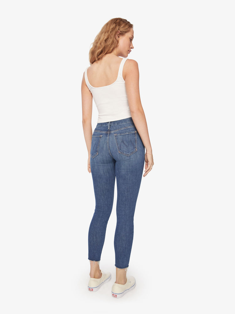 Back view of a womens mid rise jean in a medium blue wash, featuring a skinny, raw cut ankle hem.