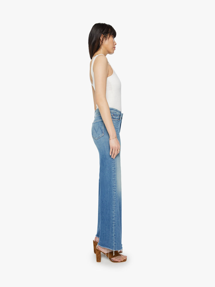 Side view of womens high waisted medium blue wash wide leg jean with a frayed hem and fading.