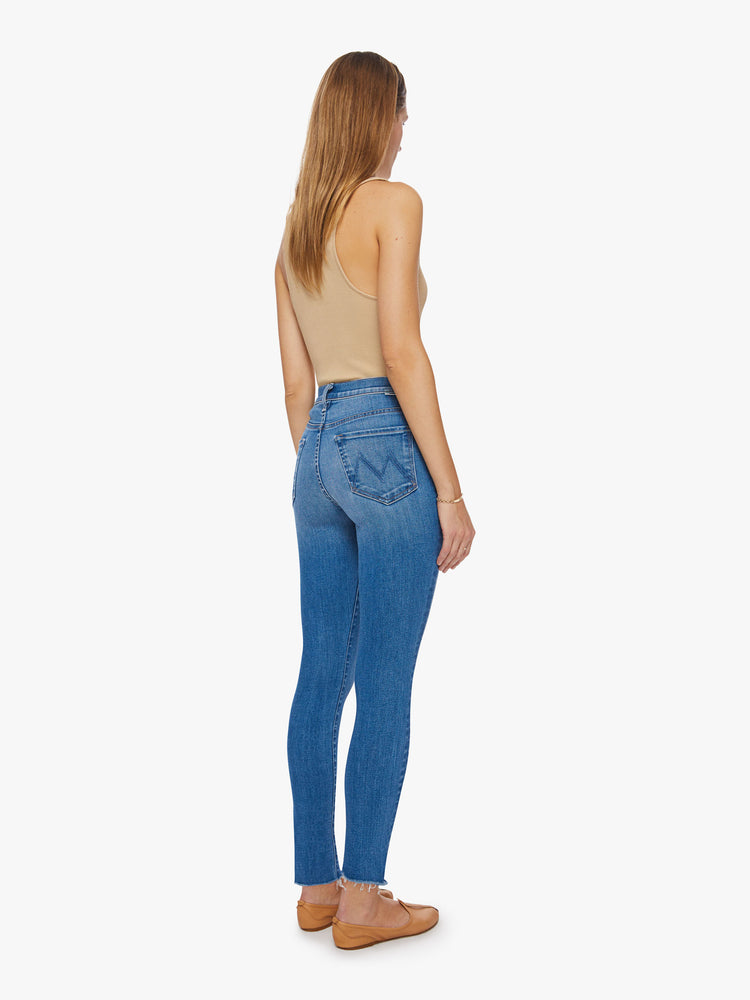 Back view of a woman high-rise skinny jean has a zip fly, ankle-length inseam and a frayed step-hem in a mid-blue wash.