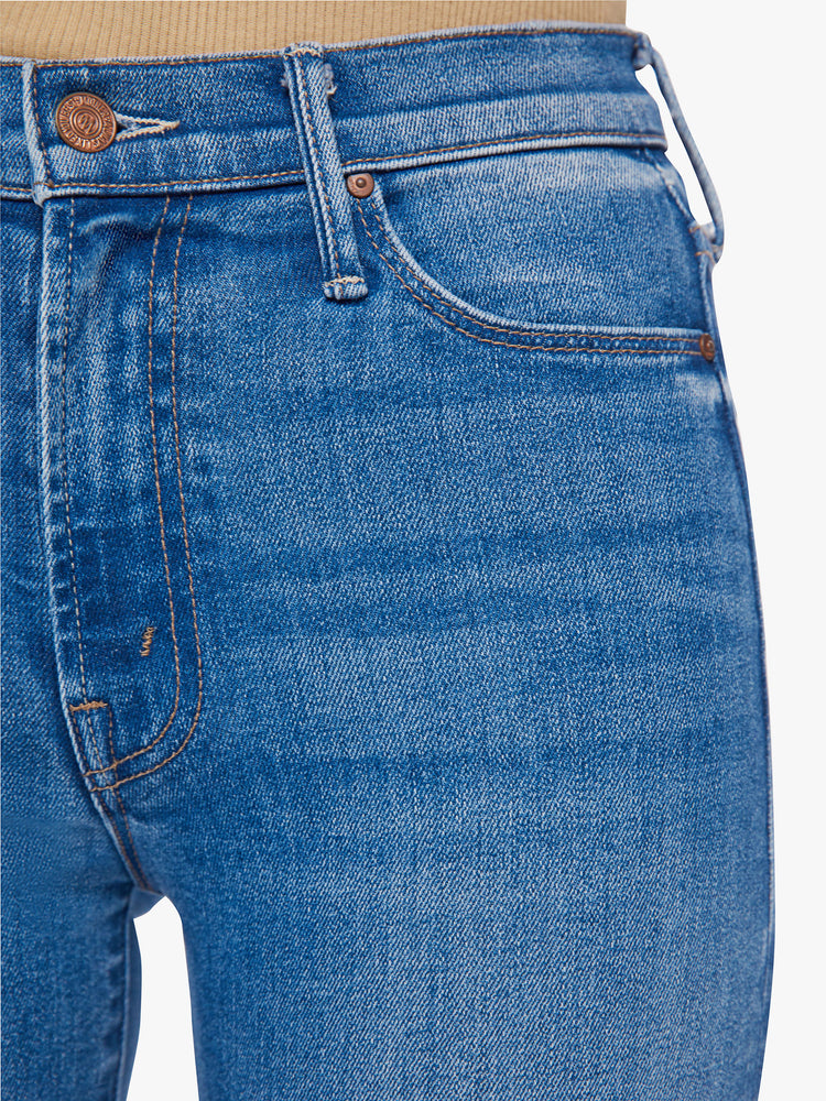 Close up view of a woman high-rise skinny jean has a zip fly, ankle-length inseam and a frayed step-hem in a mid-blue wash.
