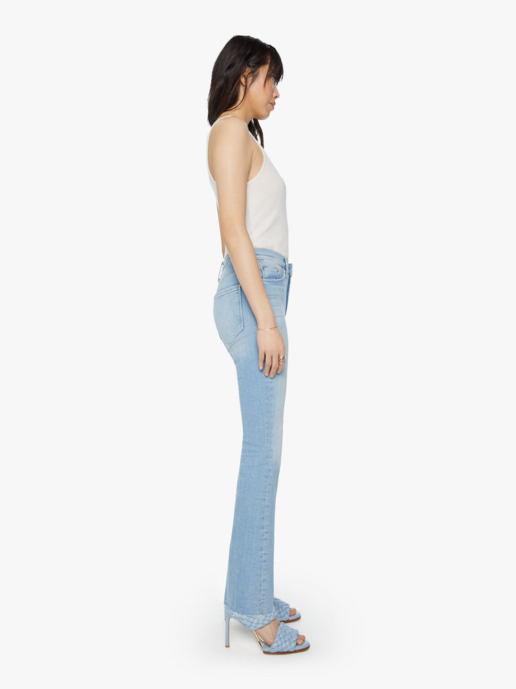 Side view of a womens mid rise flare light blue wash jean with a fading and whiskering.