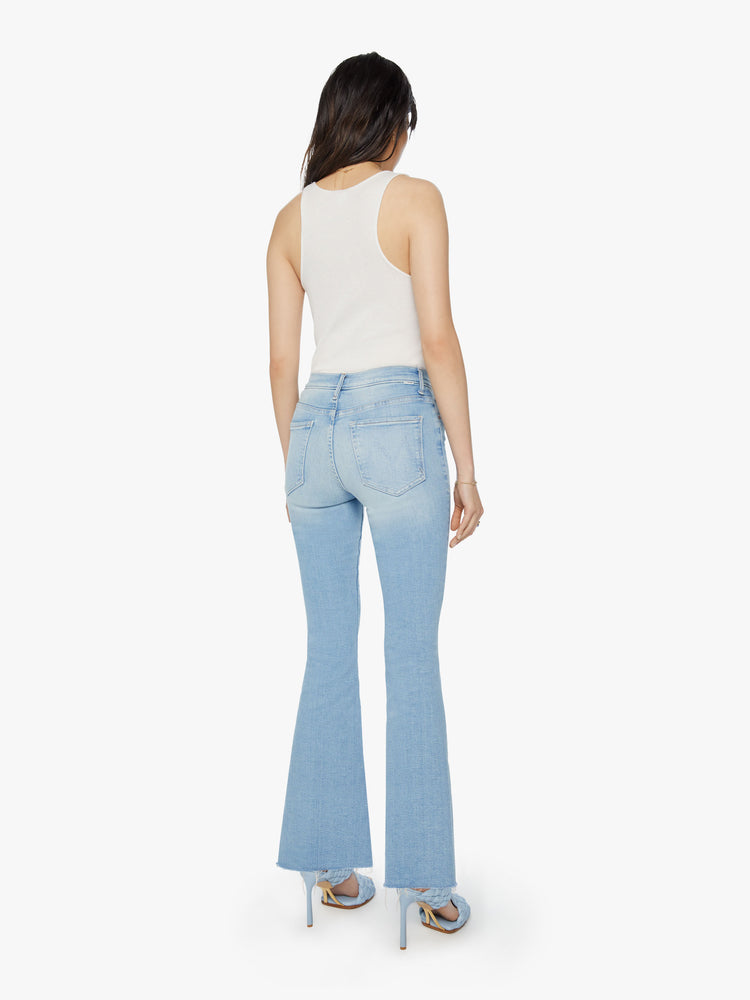 Back view of a womens mid rise flare light blue wash jean with a fading and whiskering.