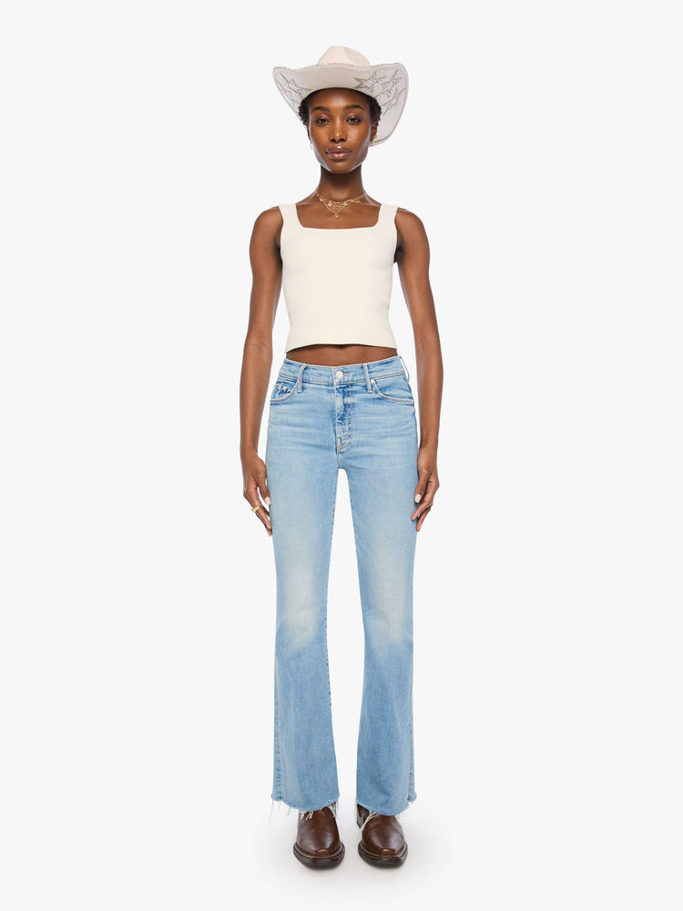 Front view of a woman in a light blue mid-rise flare has a zip fly, 31-inch inseam and a frayed hem.