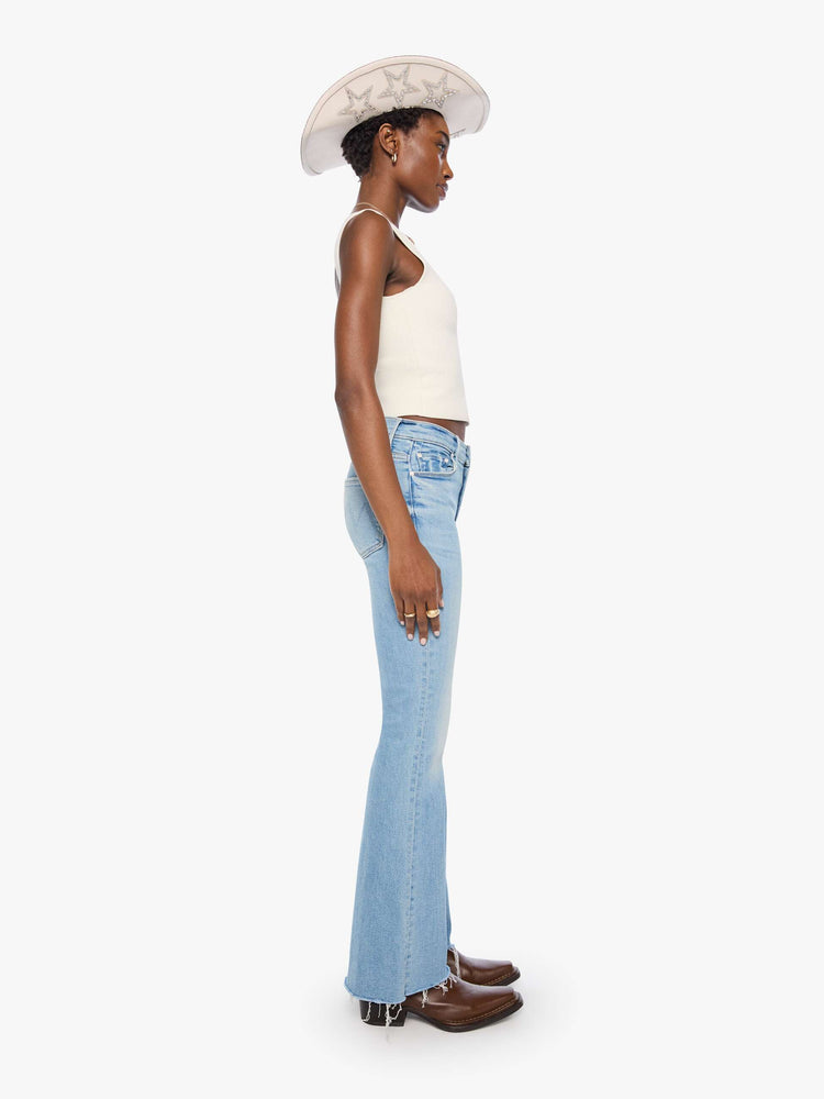 Side view of a woman in a light blue mid-rise flare has a zip fly, 31-inch inseam and a frayed hem.