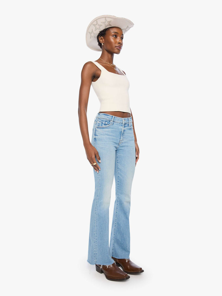 Front view of a woman in a light blue mid-rise flare has a zip fly, 31-inch inseam and a frayed hem.