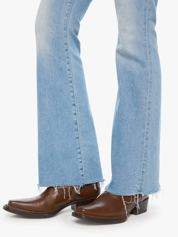 Hem view of a woman in a light blue mid-rise flare has a zip fly, 31-inch inseam and a frayed hem.