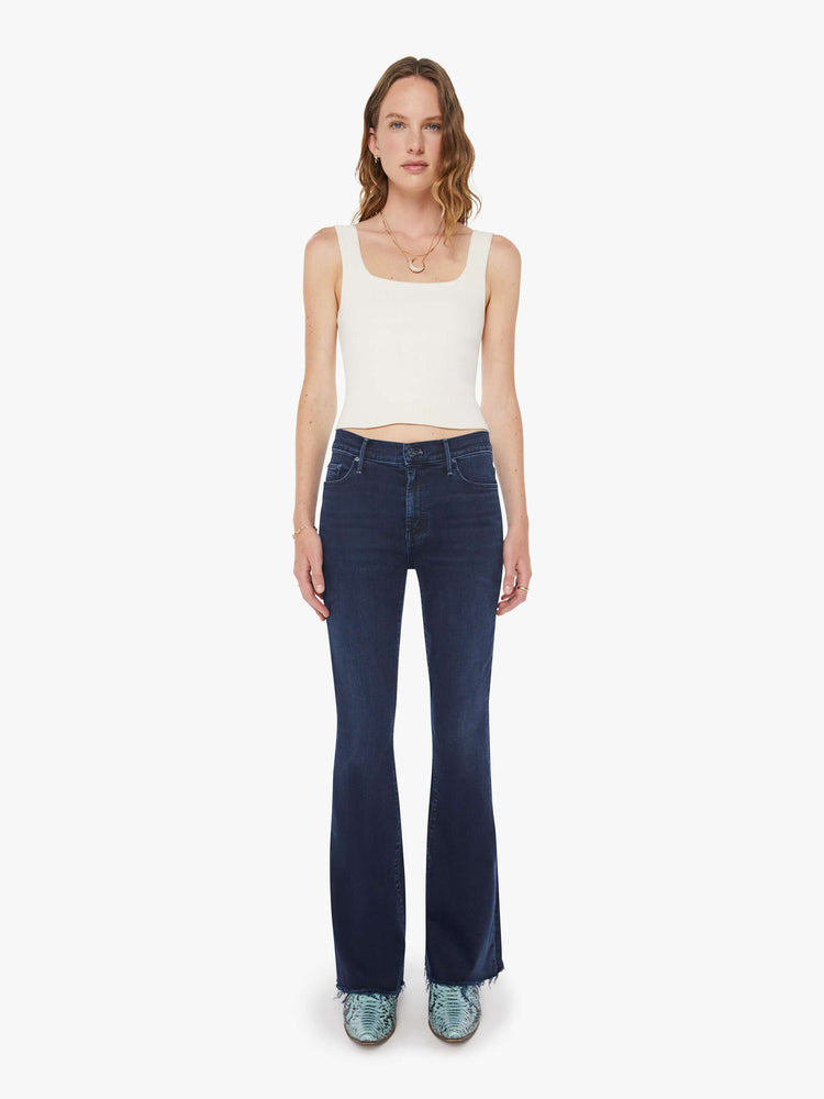 Front view of a woman in a dark blue wash mid-rise flare with a 31-inch inseam and frayed hem.