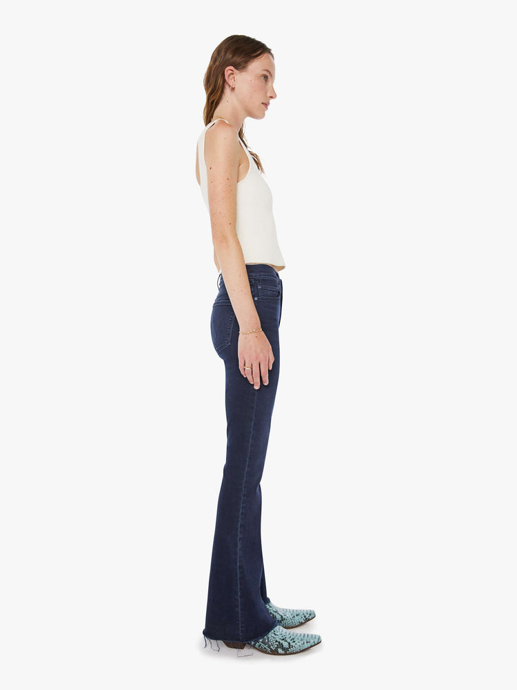 Side view of a woman in a dark blue wash mid-rise flare with a 31-inch inseam and frayed hem.