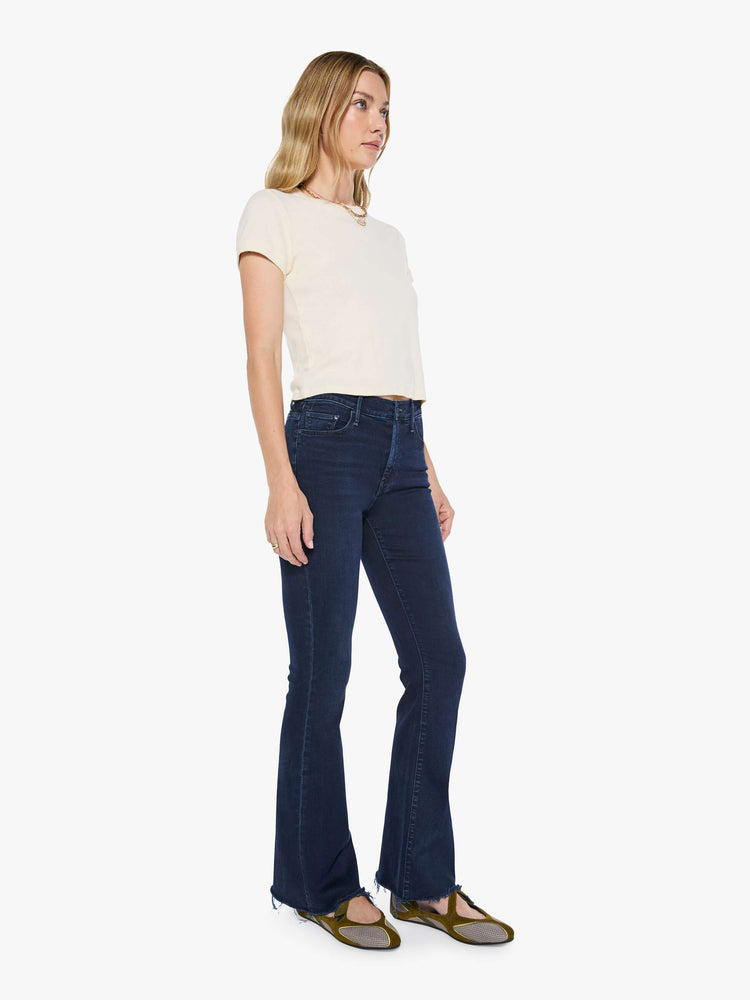 Front view of a woman in a dark blue wash mid-rise flare with a 31-inch inseam and frayed hem.